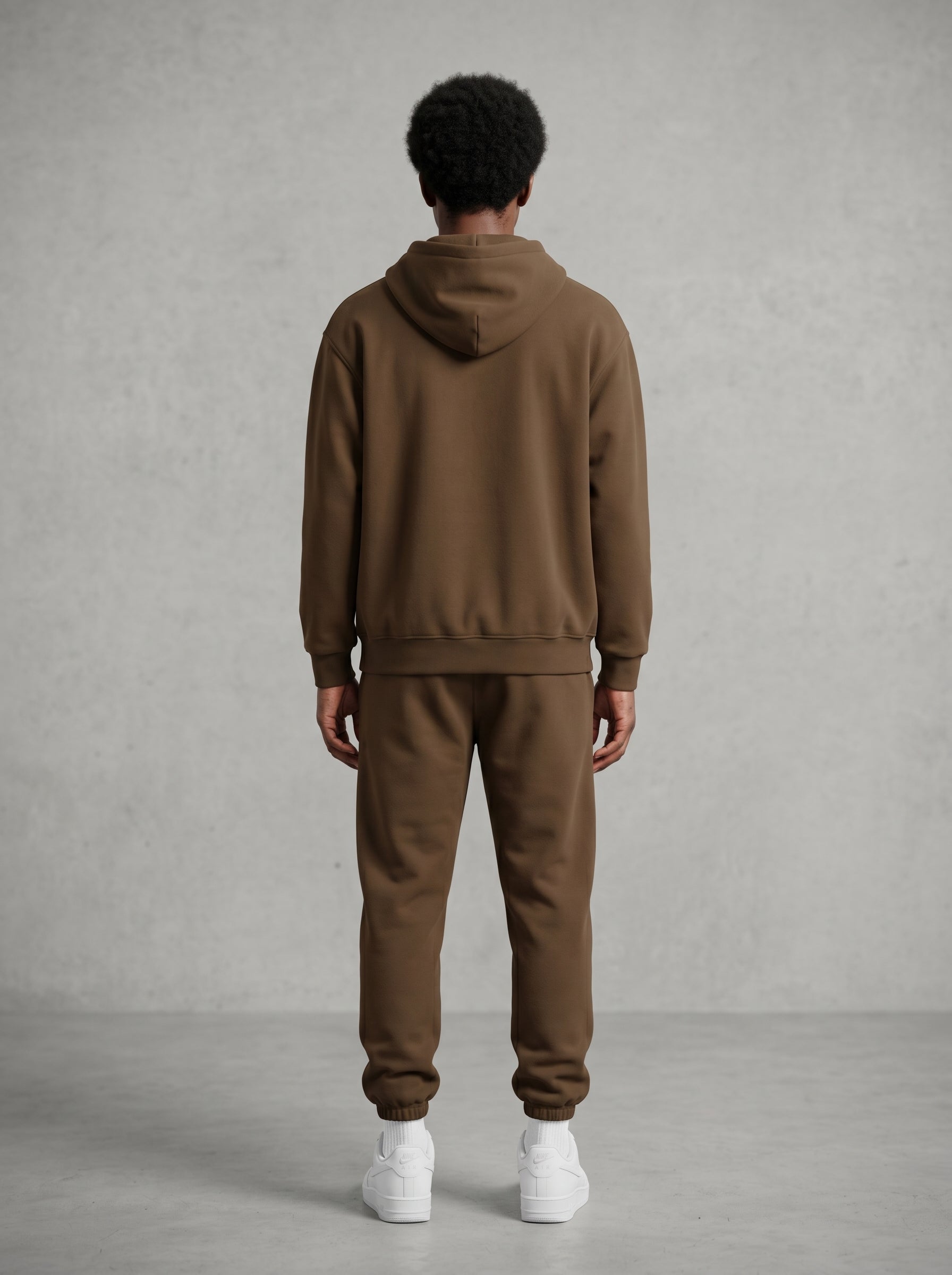 Man wearing KORTEZ coffee oversized hoodie and sweatpants set against gray wall