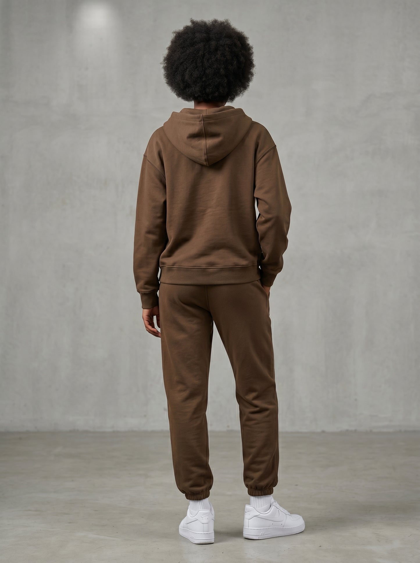 Person in KORTEZ brown hooded sweatshirt and matching pants with hand in pocket